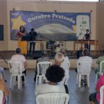 Pessoas assistem apresentação de grupo musical.